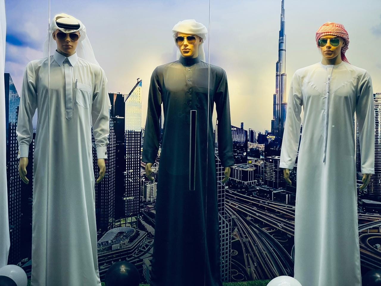 Three signature ASAYEL GENTS Qandora styles displayed against Dubai skyline